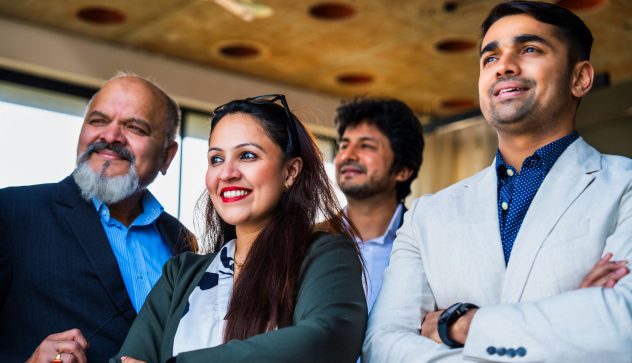 Indian Asian group of confident businessmen or corporate professionals or executives standing with arms folded, smiling, and looking directly at the camera in a modern corporate office environment