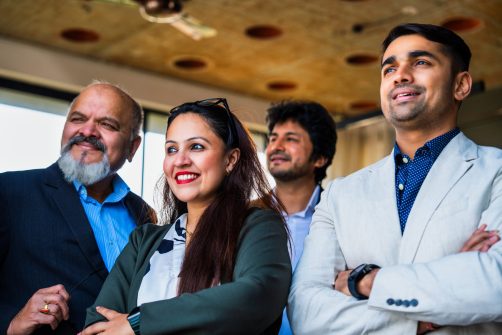 Indian Asian group of confident businessmen or corporate professionals or executives standing with arms folded, smiling, and looking directly at the camera in a modern corporate office environment